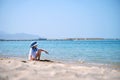 Lonely child girl playing with white sand on sea beach on background of blue sky, clear water and distant shore. Summer Royalty Free Stock Photo