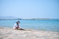 Lonely child girl playing with white sand on sea beach on background of blue sky, clear water and distant shore. Summer Royalty Free Stock Photo