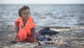 Lonely child refugee in lifejacket sitting shore, dangerous migration across sea