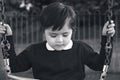 Lonely child with a sad face sitting alone on swing in the playground in black and white,School kid  with upset face playing alone Royalty Free Stock Photo