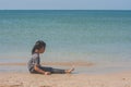 Lonely cute litle girl sitting on sand beach and looking to seascape view. Royalty Free Stock Photo