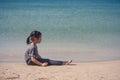 Lonely cute little girl sitting on sand beach.