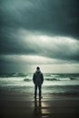 A lonely depressed man stands on a beach in the rain, looking out at the ocean