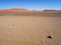 Lonely egg shape rock stone and shadow on vast empty dried desert landscape with natural sand dune curved ridge and clear blue sky