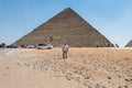 A lonely Egyptian man standing in front of Pyramid of Khufu in The Giza pyramid complex, an archaeological site on the Giza