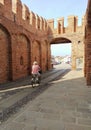 Lonely elderly woman riding a bicycle on a sunny dlia. Back view. Walking through medieval castle walls in Italy. Royalty Free Stock Photo