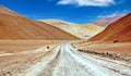 Lonely empty sandy road in hilly dry bare lonely valley between colorful desert hills, something lost curves ahead sign - Royalty Free Stock Photo