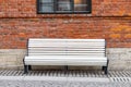 Lonely empty white wooden bench, old brown brick wall and black window on background Royalty Free Stock Photo