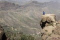 Lonely explorer on blue t shirt sitting on top of rock cliff edge Royalty Free Stock Photo