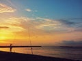Lonely fisherman on coastline. SunriSilhouette of fisherman against dramatic sky