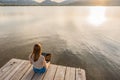 Lonely girl expressing her creativeness writing romance tales book on a wooden pier or jetty at sunset or dawn. New job