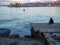 A lonely girl sits on a pier in the port. Sitting on the edge of the water