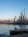 A lonely girl sits on a pier in the port. Sitting on the edge of the water. Uses a phone Royalty Free Stock Photo