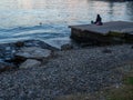 A lonely girl sits on a pier in the port. Sitting on the edge of the water. Uses a phone