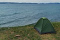 lonely green small tent stands on grass shore of blue Lake Baikal, sea waves and ripples, mountains on the horizon, summer