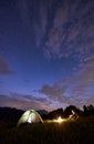 Lonely guy sitting by fire near tent on background of mountains under starry sky Royalty Free Stock Photo