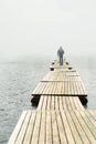 Lonely guy walking along a long wooden bridge on a lake stretching into fog