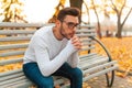 A lonely handsome man sits sad in the park on a bench. Autumn season, yellow leaves on background.