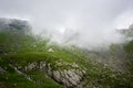 Lonely house isolated in green beautiful rocky meadow near magnificent grassy mountains covered in fog in Romania. Royalty Free Stock Photo