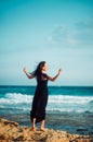 Lonely inspired woman in black dress staying on seaside dreaming and looking to sea on windy sunset day. Back view. Emotions Royalty Free Stock Photo