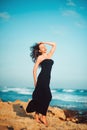 Lonely inspired woman in black dress staying on seaside dreaming and looking to sea on windy sunset day. Emotions loneliness