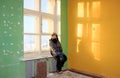 Lonely kid girl in abandoned old children school, oldish walls with cracked painter yellow blue green walls, forsaken strange left