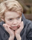 Lonely kid with his hands on his chin thinking. Young little teen kid outside on a playground alone. Cute caucasian male