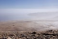 Lonely lifeless lake shore in early morning with soft haze above water and pebble coast with cape in fog. Mysterious and unearthly