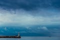 Lonely lighthouse with a red lantern on a background of rainy blue clouds Royalty Free Stock Photo