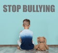 Lonely little boy with toy sitting on floor near wall. Message STOP BULLYING Royalty Free Stock Photo