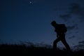 lonely man with backpack during night outdoors hiking in hills with blowing wind and shining moon and clouds with copy