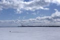 A lonely man crossing with a bag in his hand a frozen sea from one shore to another in wintertime with industrial factories and Royalty Free Stock Photo