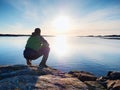 Lonely man hiker sits alone on coast and enjoying sunset. View over rocky cliff to ocean