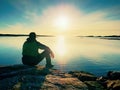 Lonely man hiker sits alone on coast and enjoying sunset. View over rocky cliff to ocean