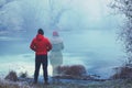 Lonely man in red jacket standing by the lake in winter, with transparent woman figure standing next to him Royalty Free Stock Photo