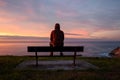 Lonely man sits alone on the rocky coast and enjoying sunset.