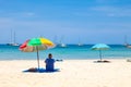 A lonely man sits under a colored umbrella in the shade from the hot sun on nai harn beach, thailand during vacation and travel.