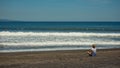 Lonely man is sitting on black sand at the beach. Royalty Free Stock Photo