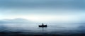 A lonely man sitting in a boat in the middle of a vast lake. Overcast, foggy wheather