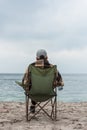lonely man sitting on chair at seashore on cloudy