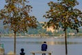 Lonely man sitting between two trees on a bench and looking at the lake. In the distance you can see the island on which stands th Royalty Free Stock Photo