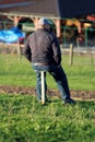 Lonely man with sport hat sitting on improvised wooden chair overlooking houses in distance on top of small hill covered with