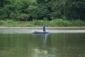 Lonely man stands on the boat and collects the fish from the net with forest in background