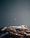 Lonely man on the top of a snow-capped mountain admiring the daytime half-moon during sunset Royalty Free Stock Photo