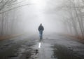 Lonely man walking in fog away road. Rural landscape with road in morning mist. Warm autumn colors. Dark mysterious background Royalty Free Stock Photo