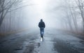 Lonely man walking in fog away road. Rural landscape with road in morning mist. Warm autumn colors. Dark mysterious background Royalty Free Stock Photo