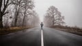 Lonely man walking in fog. Rural landscape with road in morning mist. Warm autumn colors. Dark mysterious background Royalty Free Stock Photo