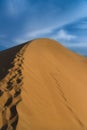 Lonely Man Walks Along The Crest Of A Huge Sand Dune Against The Blue Cloudy Sky, Leaving Behind Him Traces On The Sand. Footprint