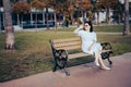 Lonely middle-aged woman sits alone on a bench in a park area on the waterfront. wearing a white dress and sunglasses. an adult Royalty Free Stock Photo