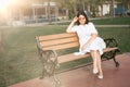 Lonely middle-aged woman sits alone on a bench in a park area on the waterfront. wearing a white dress and sunglasses. an adult Royalty Free Stock Photo